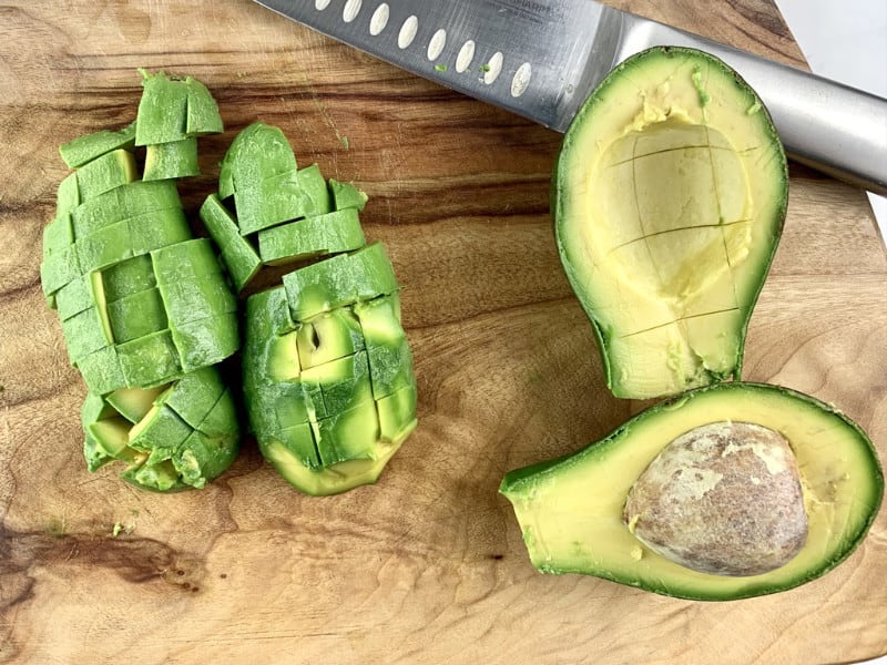 Close-up of diced shephard avocados on a wooden board with knife.