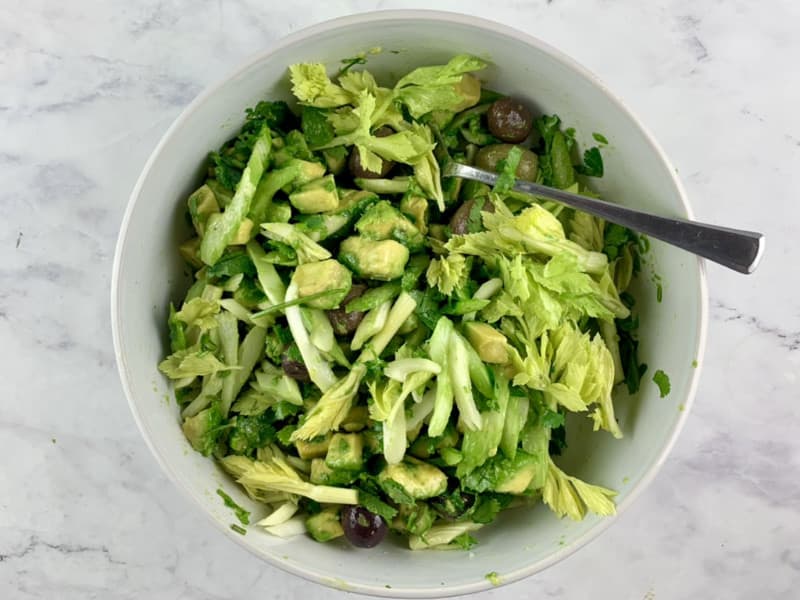 Mixing celery avocado salad in a white bowl with a spoon.