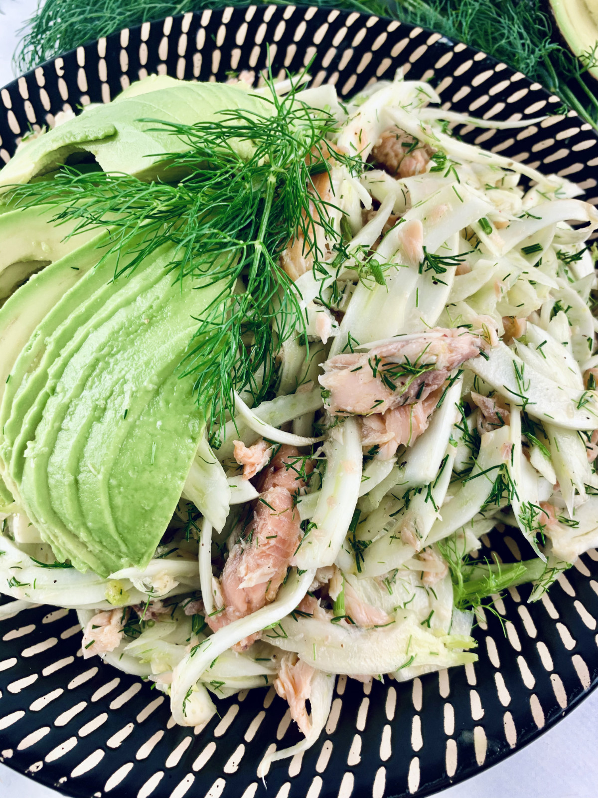 Close-up of Smoked trout & fennel salad on a patterned platter with dill & avocado on the side.