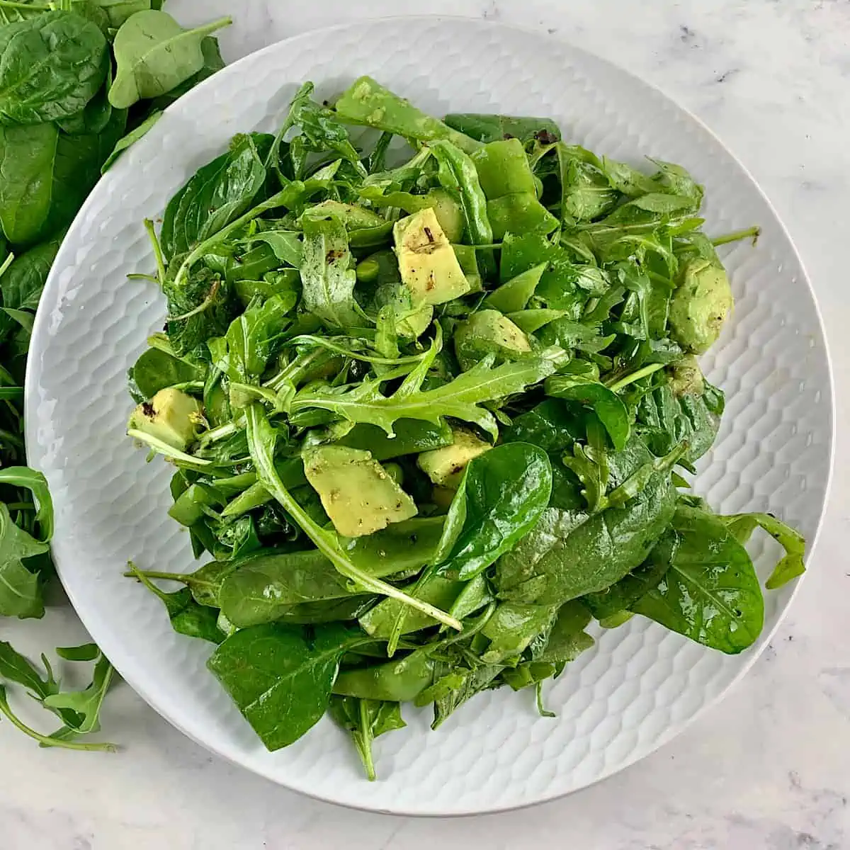 Spinach arugula salad on a white plate with greens scattered around.