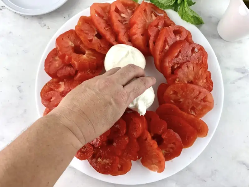 Arranging burrata onto a platter with sliced tomatoes.