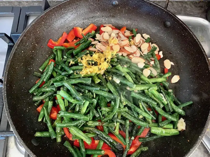 Snake beans, capsicum strips, flaked almonds and lemon zest in pan.
