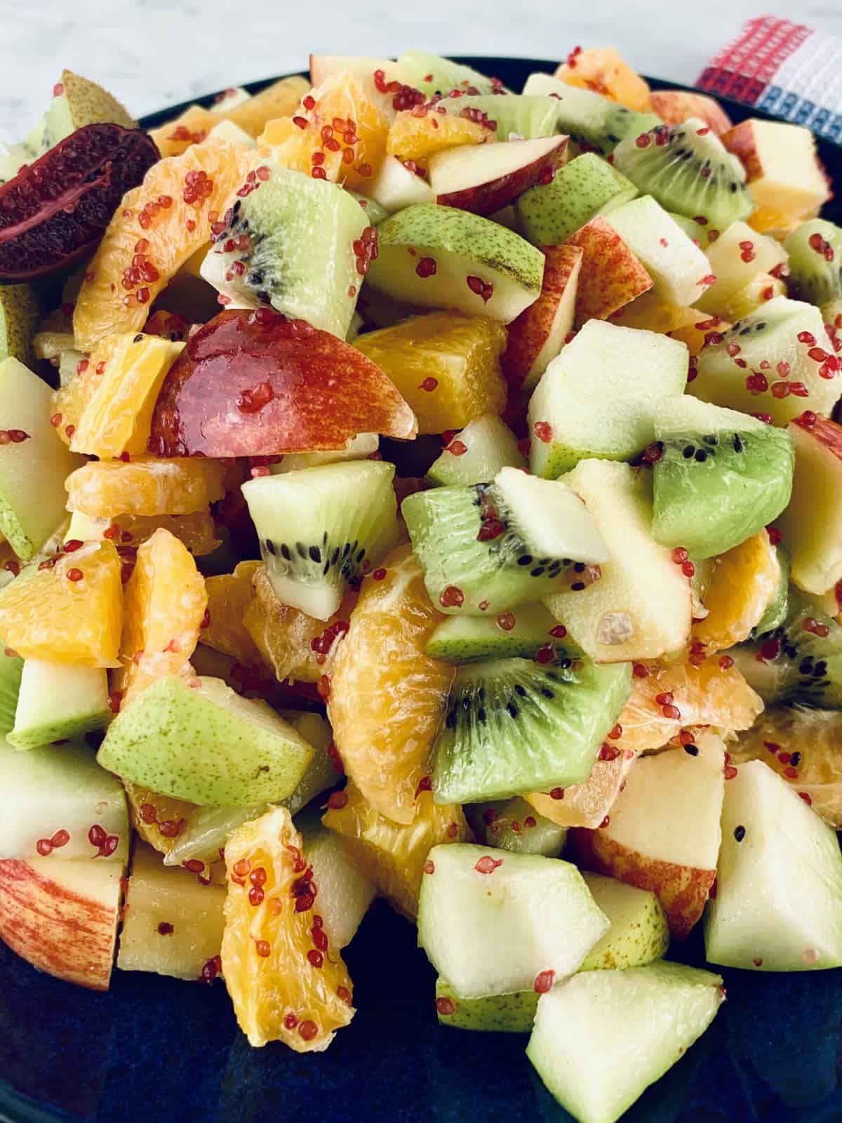 A closeup of Autumn fruit salad on a black plate on top of a checked tea towel.