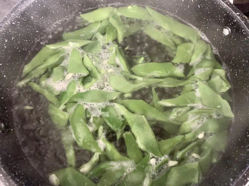 Flat beans boiling in a pot of salted water.