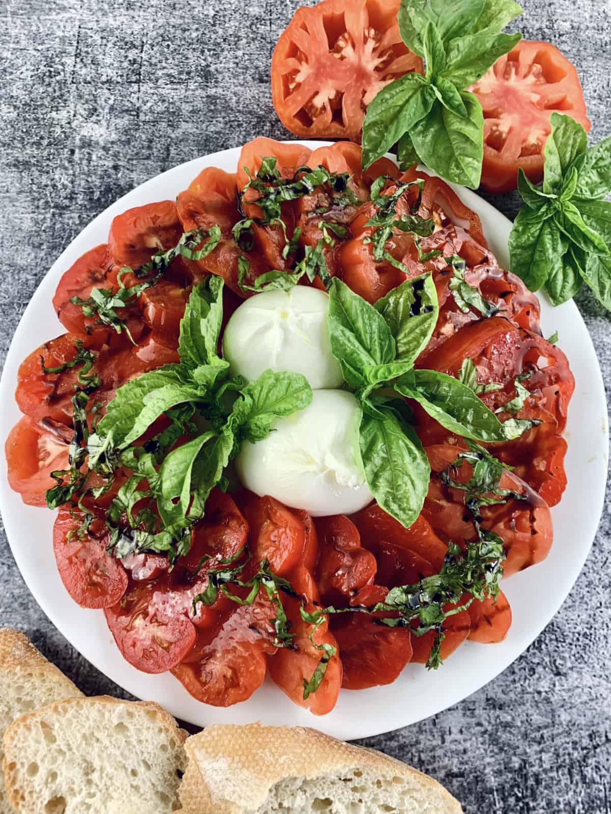 Burrata caprese salad with sliced tomatoes, bresh bread and basil sprigs on the side.