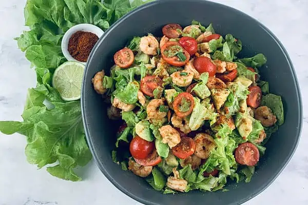 Cajun shrimp salad in a dark grey bowl with lettuce, lime & Cajun spice on the side.