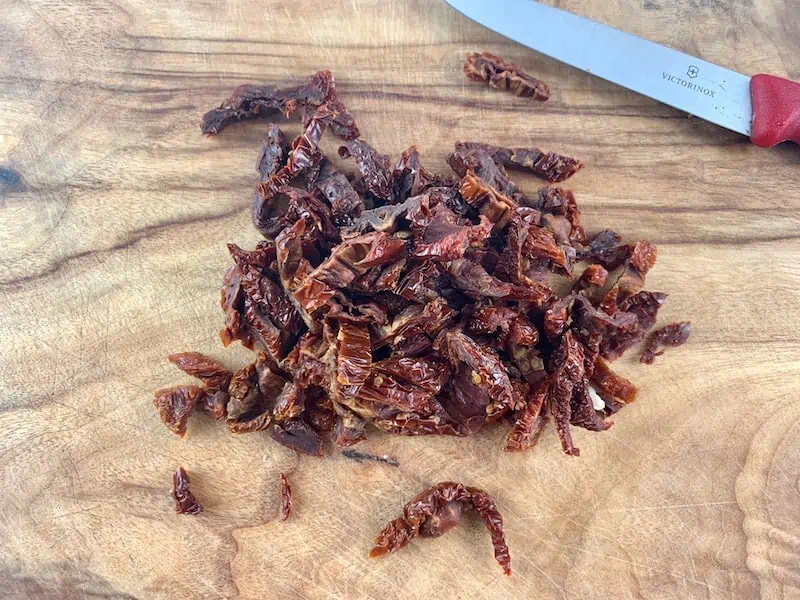 Dried tomato strips on a wooden board with a knife on the side.