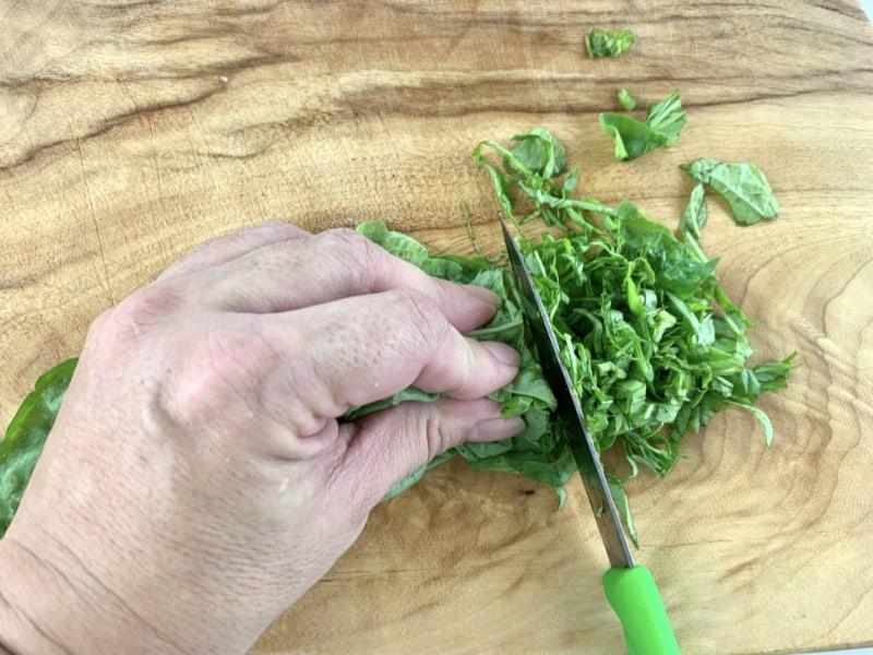 Hands slicing the basil into chiffonade ribbons.