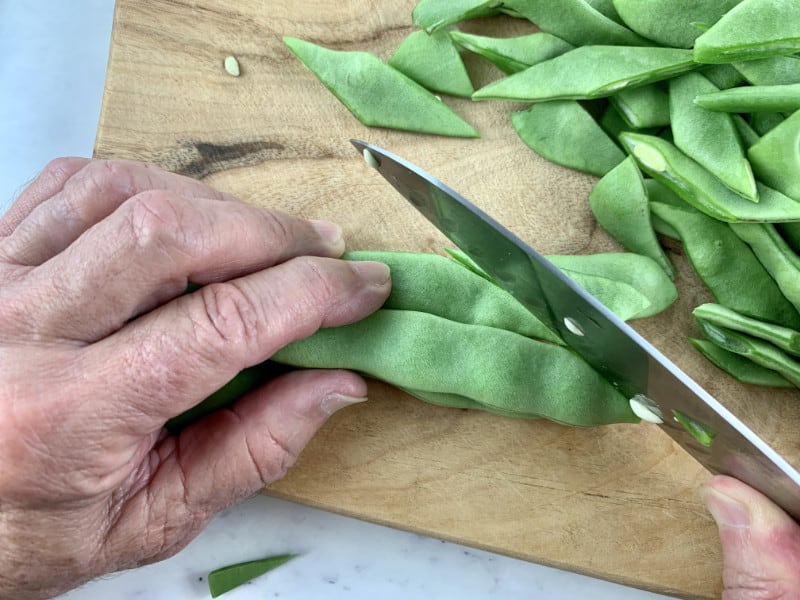 Hands cutting flat beans on the diagonal.