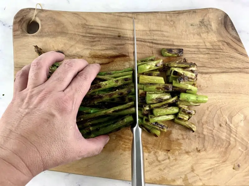 Hands cutting grilled asparagus spears on a wooden board.