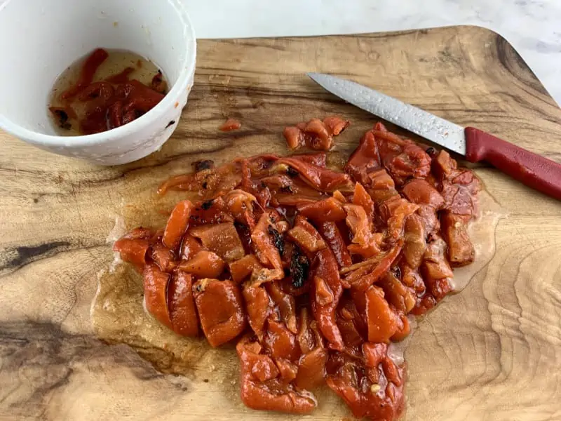 Diced jarred red peppers on a wooden board.