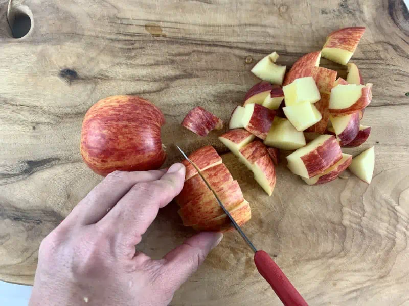 Hands dicing red apple on wooden board.