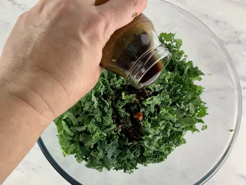 Pouring pomegranate dressing over chopped kale in a bowl.