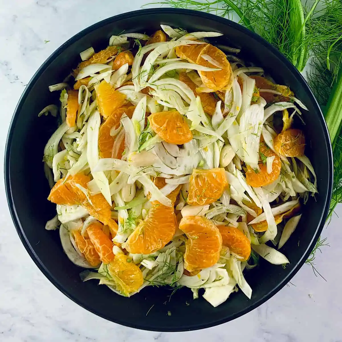 Fennel Mandarin Salad in a black bowl with fennel on the side.