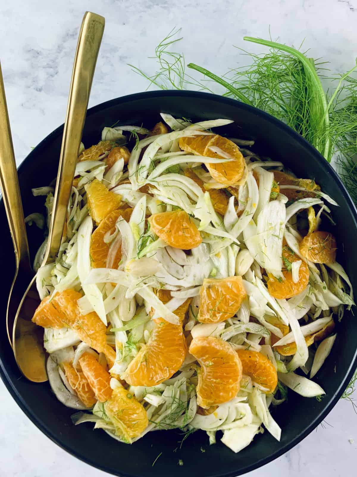 Fennel Mandarin Salad in a black bowl with fennel and gold servers on the side.