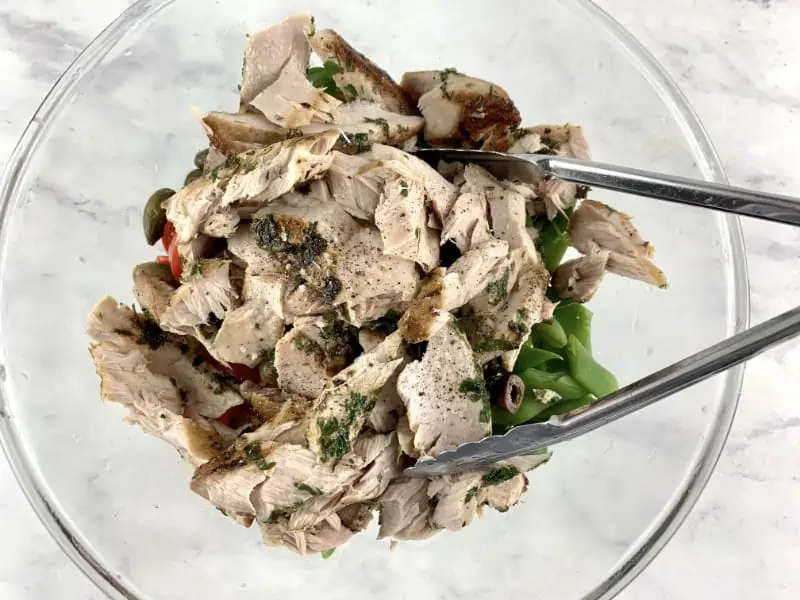 Flaked tuna on top of fresh tuna salad ingredients in a bowl with tongs.