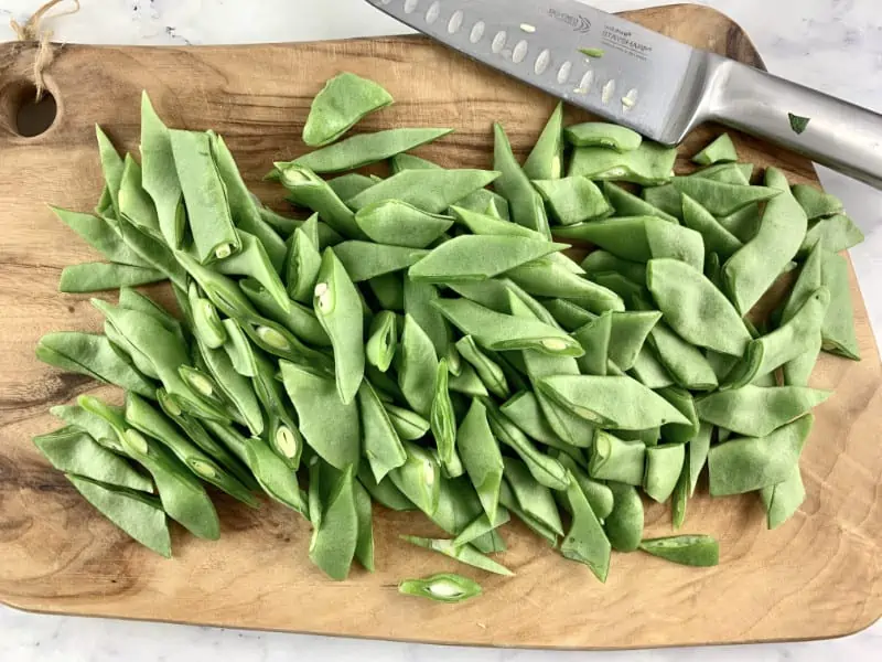Diagonally cut flat beans on a wooden board with a knife.