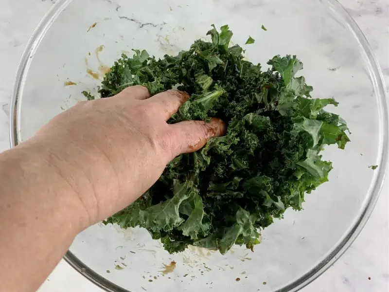 Hands massing kale with pomegranate dressing in a bowl.