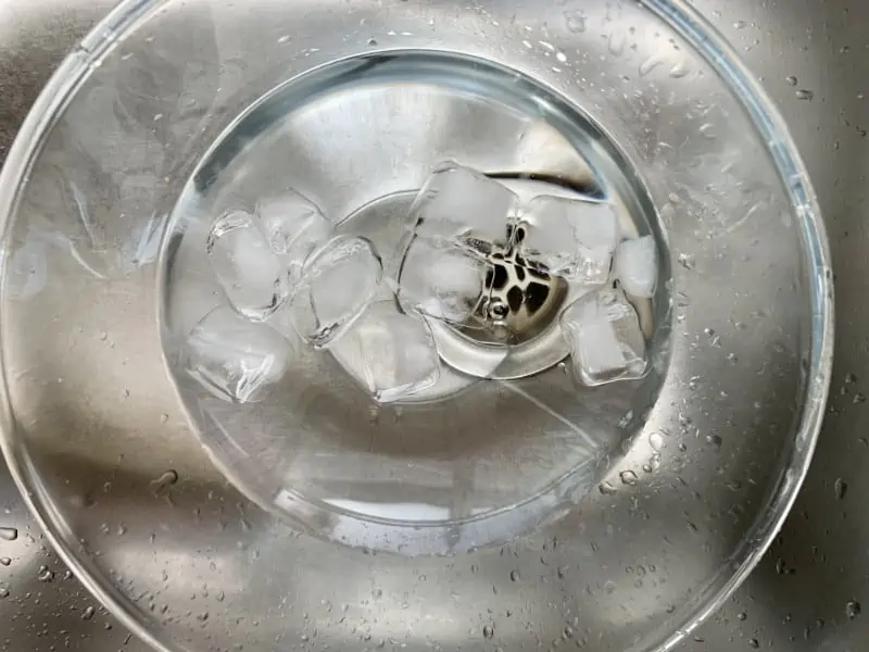 Ice and water in a glass bowl in the sink.