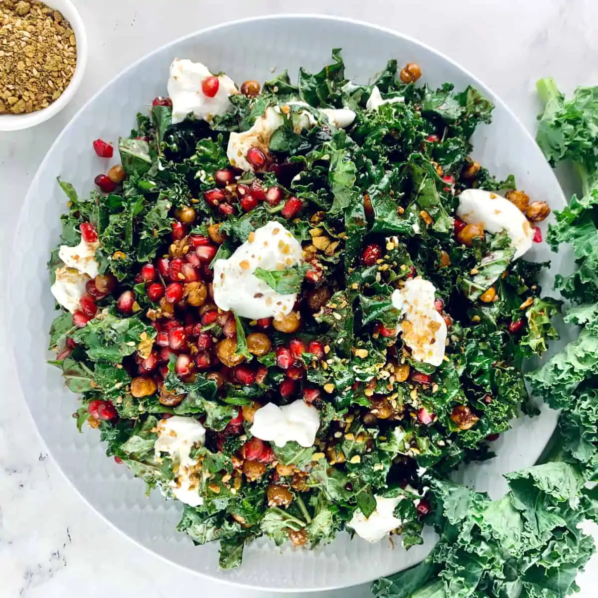 Kale pomegranat salad on a white plate with kale and dukkah on the side.