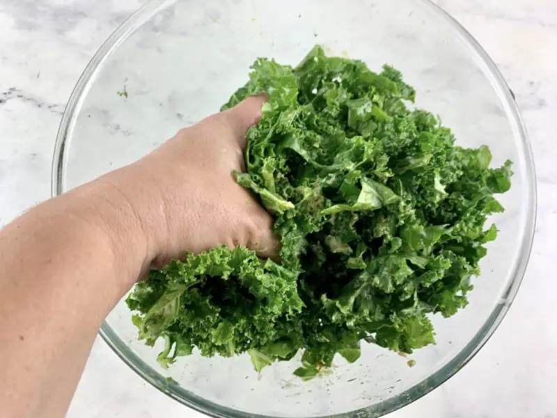 Hands massaging kale and pesto to soften it.