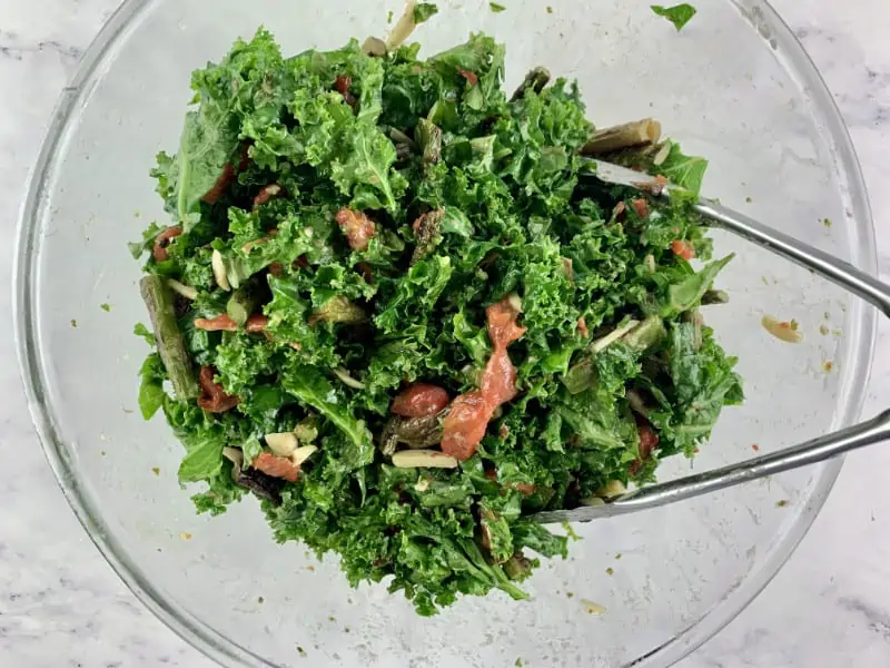Mixing asparagus kale salad in a glass bowl with tongs.