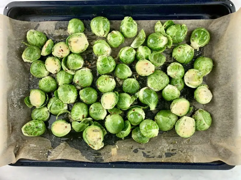 Oiled and seasoned cut sprouts on a lined baking tray.