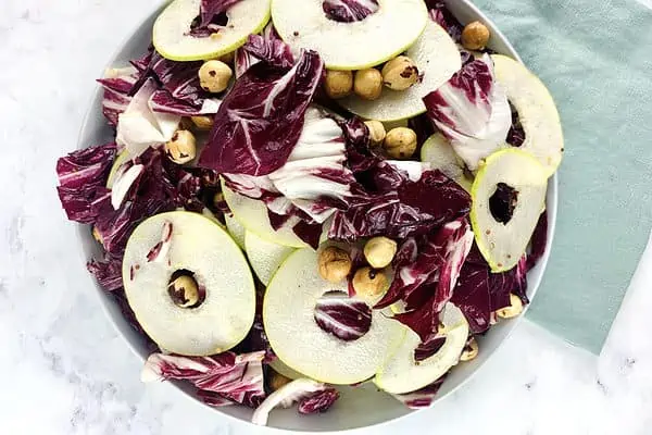 Radicchio and pear salad in a white bowl with a linen mint towel on the side.