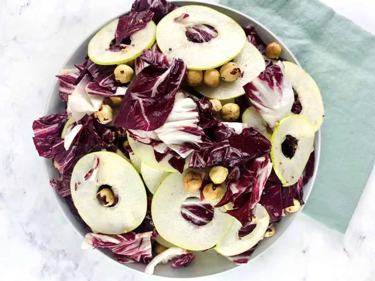 Radicchio and pear salad in a white bowl with a linen mint towel on the side.