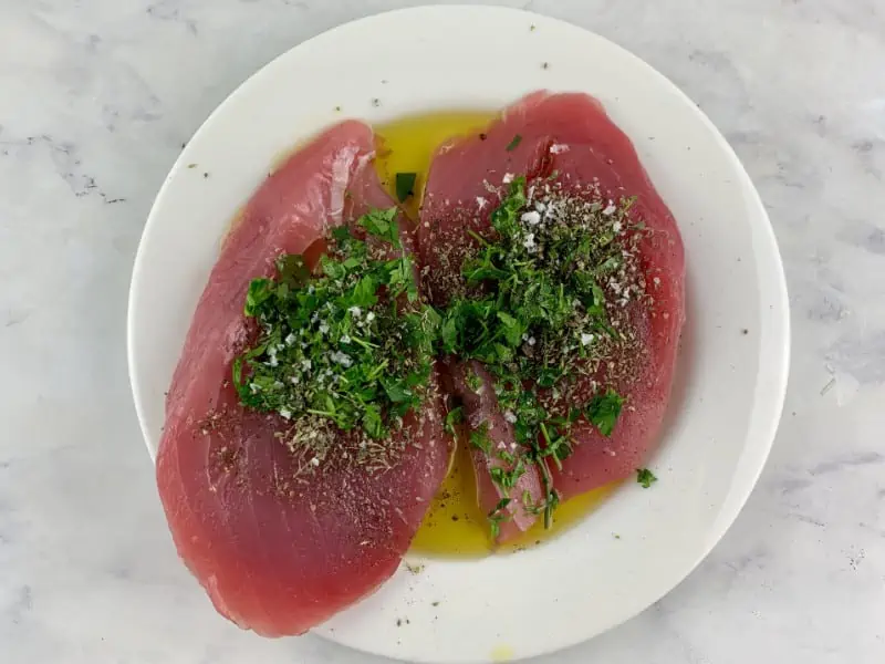 Tuna steaks on a plate with marinade ingredients.