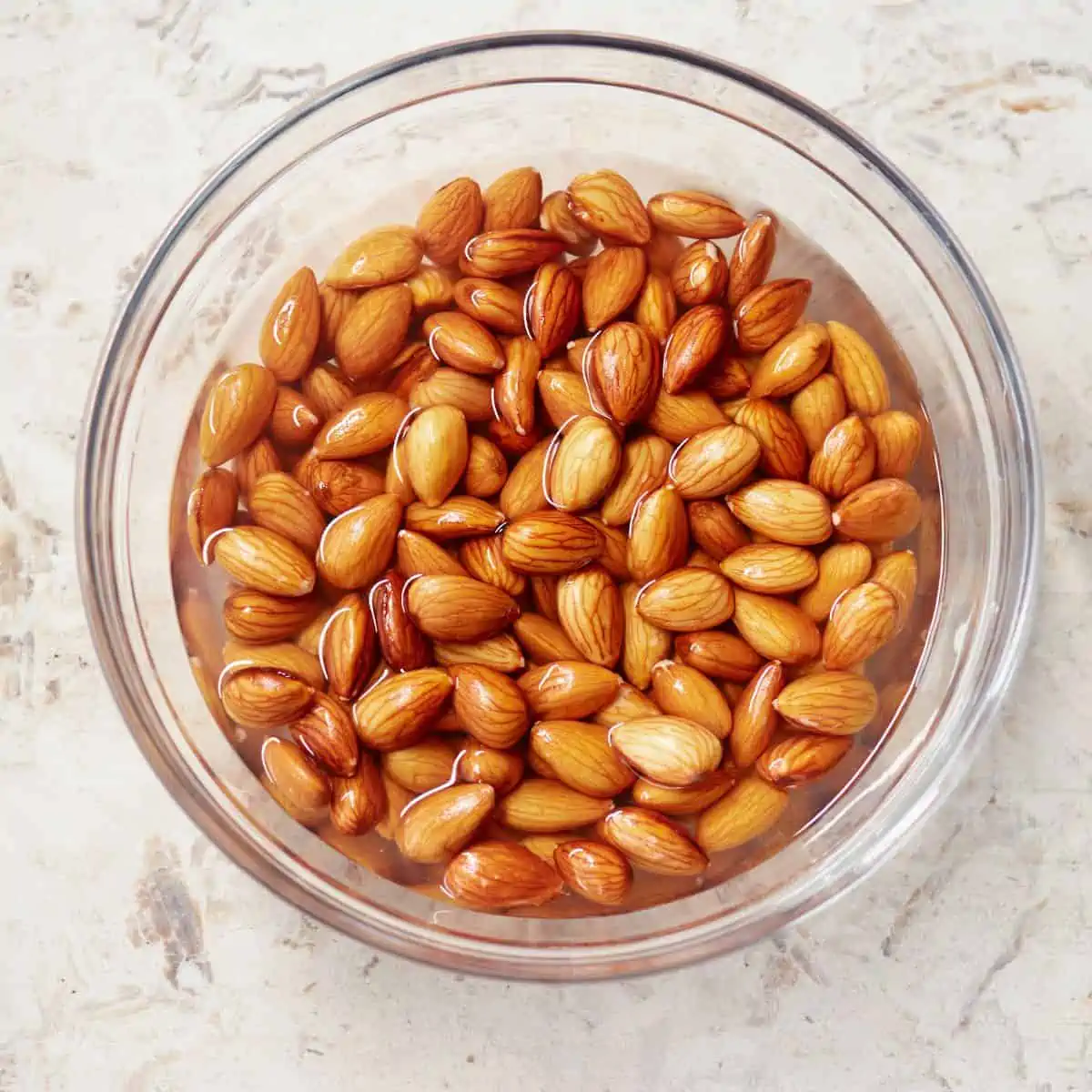 Whole almonds soaking in hot water in a glass bowl.