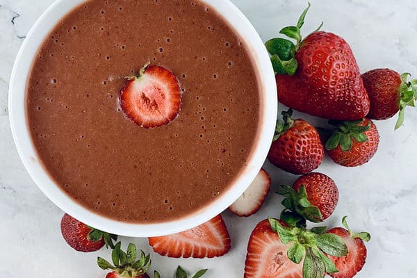 Strawberry balsamic dressing in a white bowl with strawberries around it.