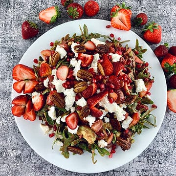Strawberry Goat Cheese Salad on a white platter with scattered strawberries.