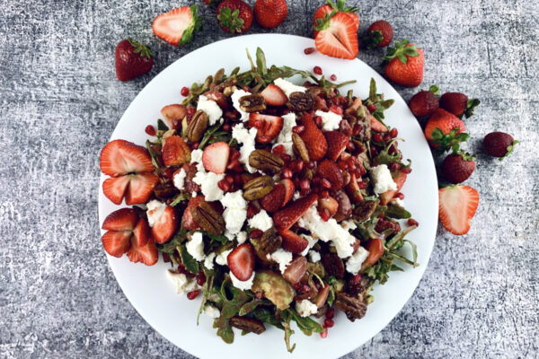 Strawberry Goat Cheese Salad on a white platter with scattered strawberries.
