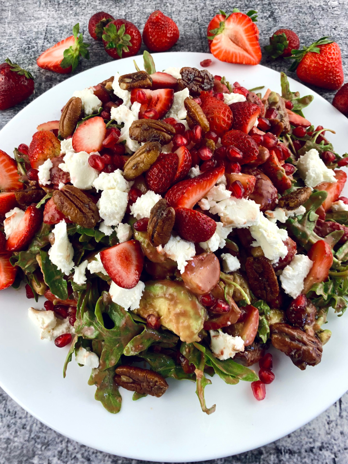 A close up of strawberry goat cheese salad on a white plate with scattered strawberres.