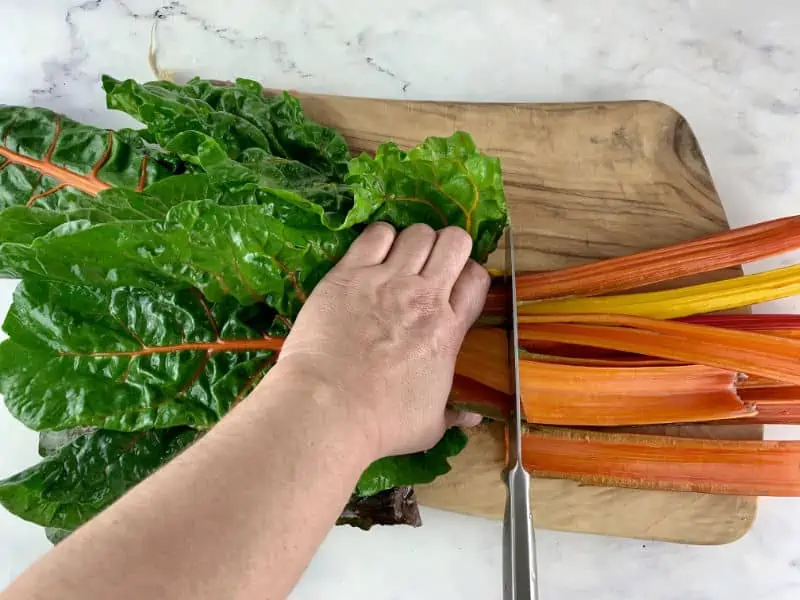 Hands cutting chard stalks on a wooden board.