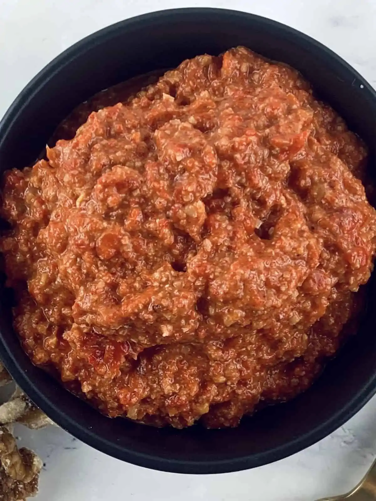 Our Lebanese Muhammara recipe in black bowl with gold spoon and walnuts on the side.