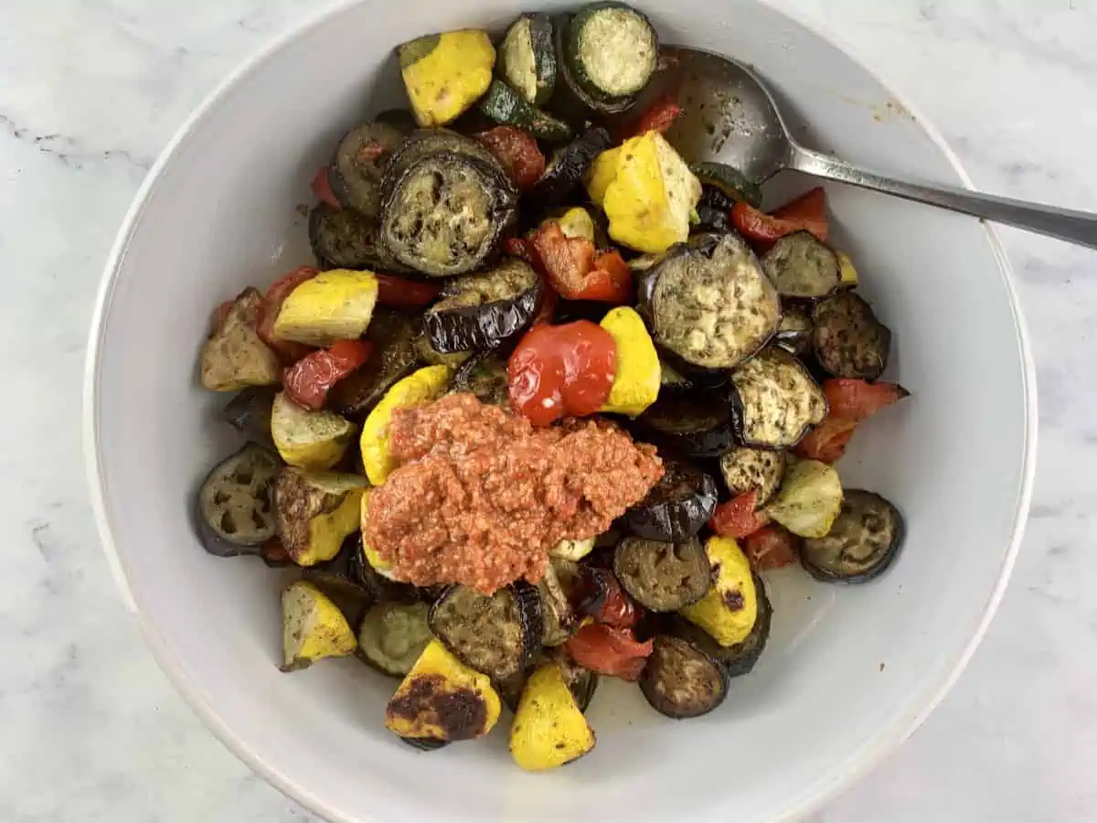 Roasted summer veg in a white bowl with Muhammara.