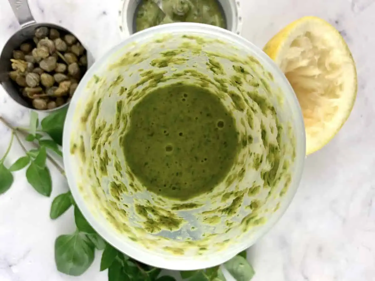 Blitzed basil caper dressing in a blender with ingredients scattered around. 