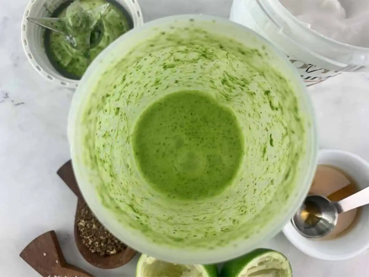 Blitzed Green goddess dressing ingredients in blender with ingredients scattered around.