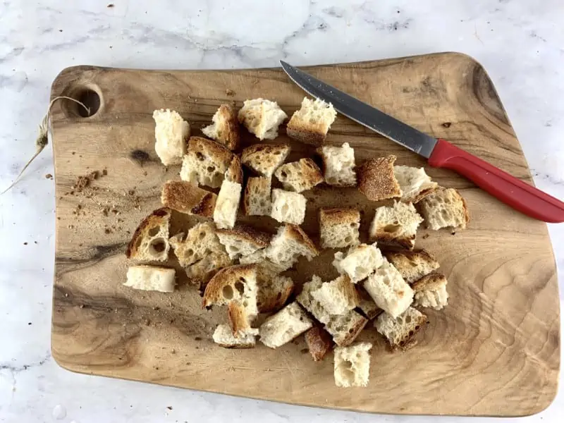 Diced bread croutons on wooden board with a red knife.