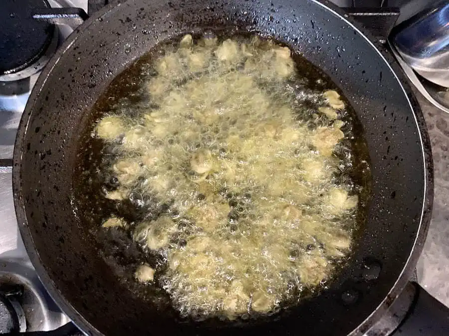 Capers in oil frying in a pan on the stove. 