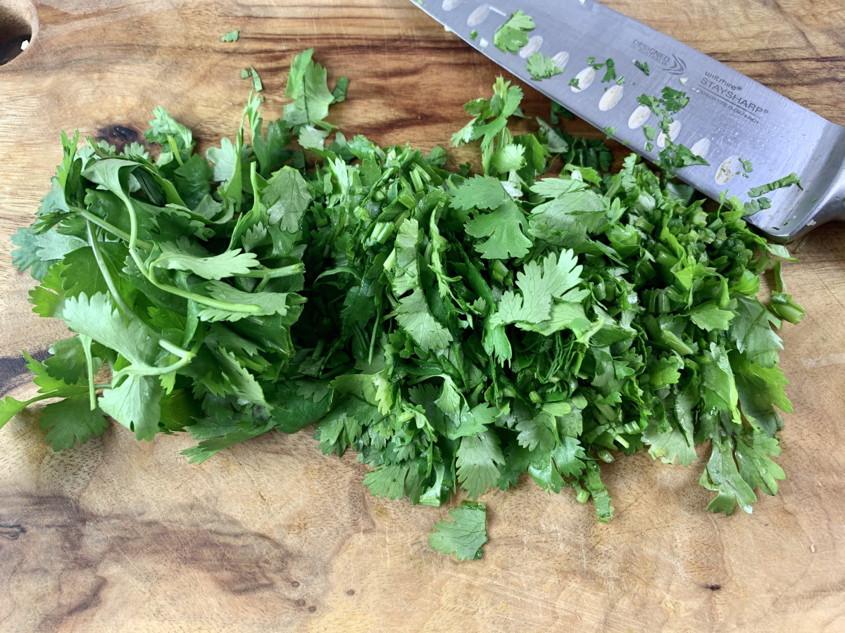Chopped coriander, cilantro, on a wooden board with a knife.
