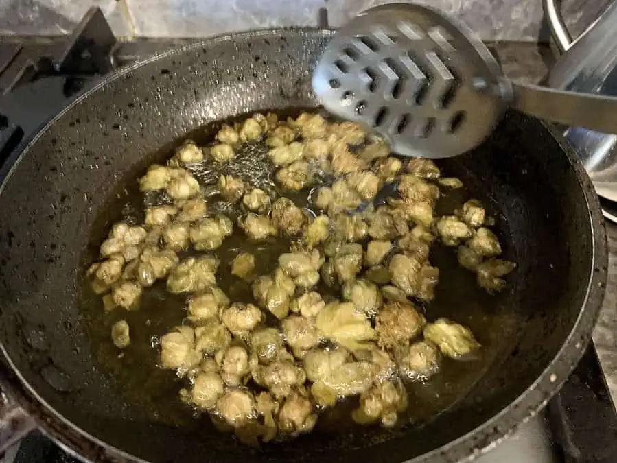 Turning fried cpaers with a slotted spoon in pan.