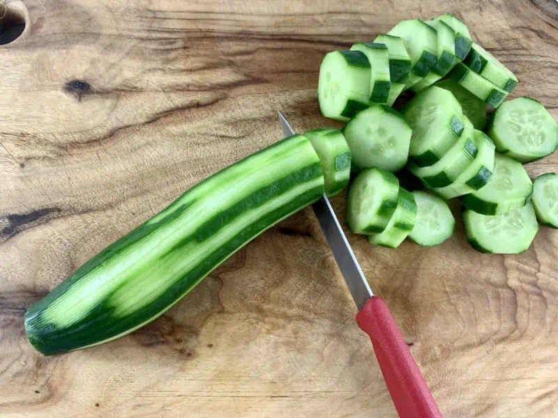Cutting cucumber rounds with a knife on a wooden board.