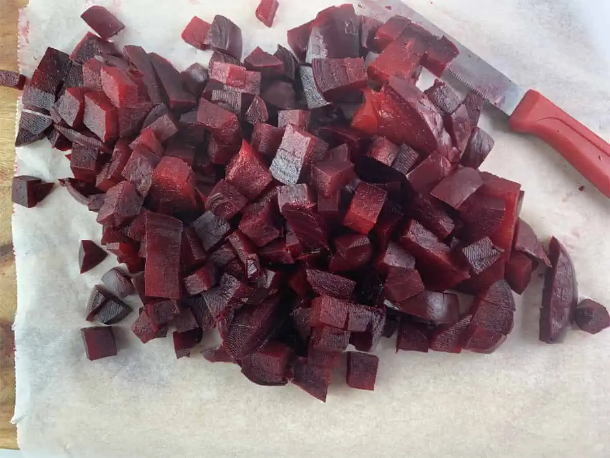 Diced beets on a wooden board lined with baking paper and a knife on the side.