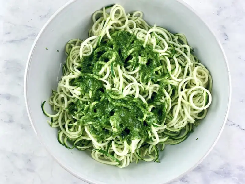 Dressing over zoodles in a white bowl.