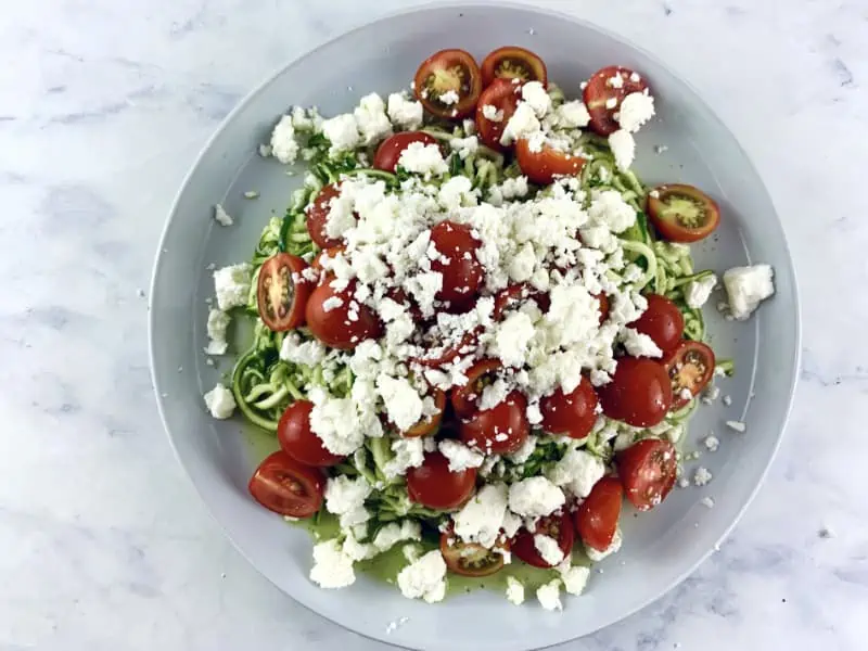 Dressed zoodles on a platter with tomatoes and feta.