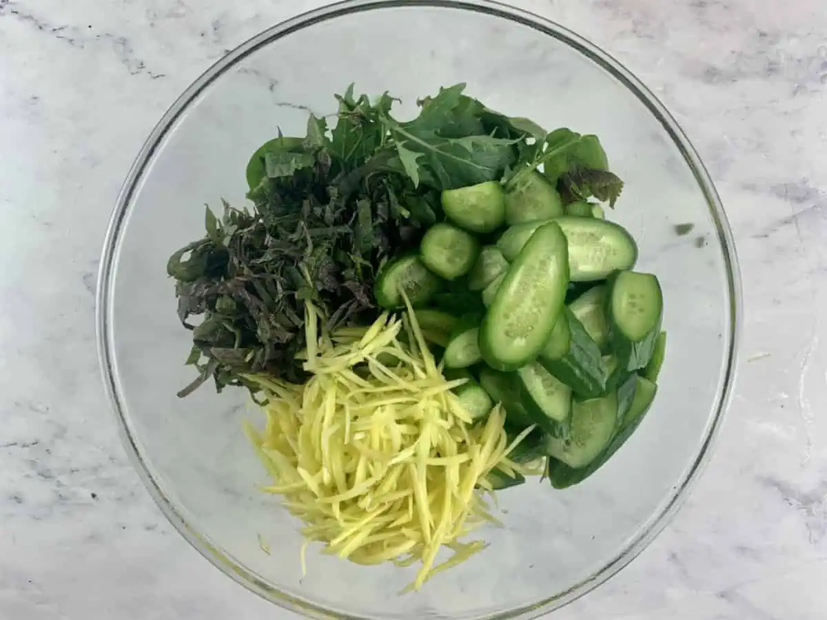 Prepared green mango salad ingredients in a glass bowl.