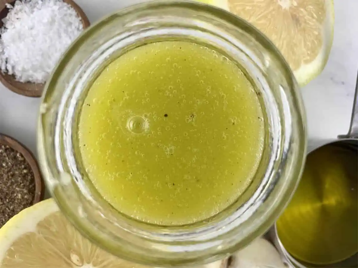 Shaken lemon garlic vinaigrette in a glass jar with ingredients scattered around.